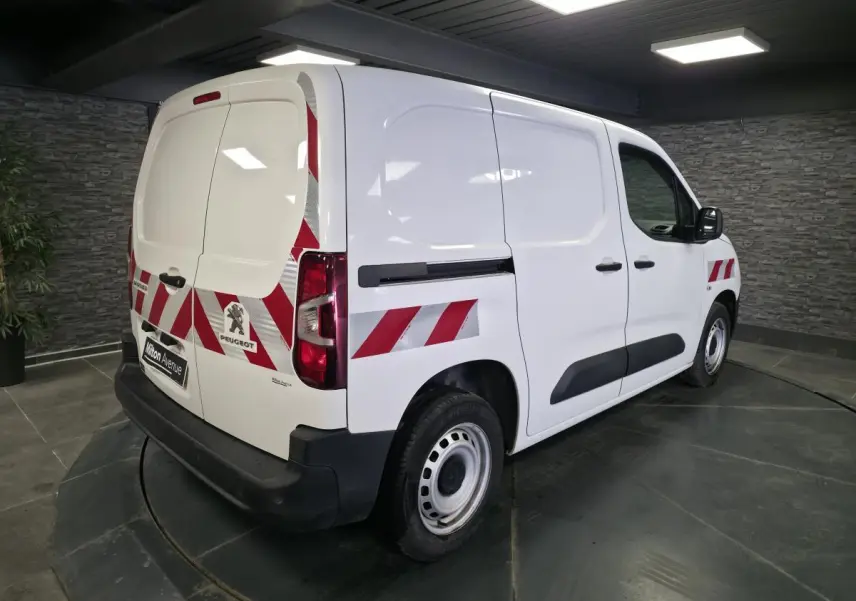Vue 3/4 arrière droite d’un Peugeot Partner blanc avec bandes réfléchissantes rouges et protections noires.