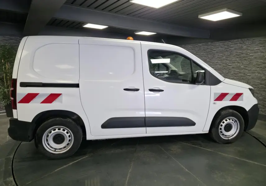 Vue latérale droite d’un Peugeot Partner blanc avec bandes réfléchissantes rouges et éléments noirs sur les portes.