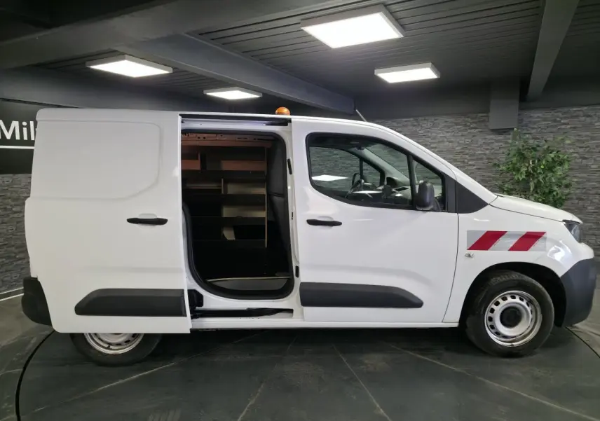 Vue latérale droite d’un Peugeot Partner blanc avec porte coulissante ouverte et bandes rouges diagonales sur l’aile avant.