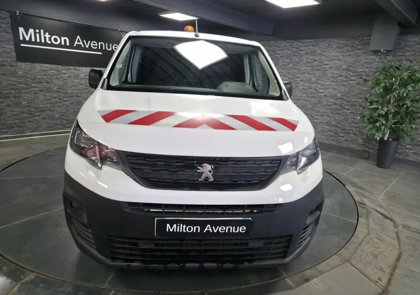 Vue avant d'un Peugeot Partner blanc avec bandes rouges diagonales sur le capot, en intérieur showroom.