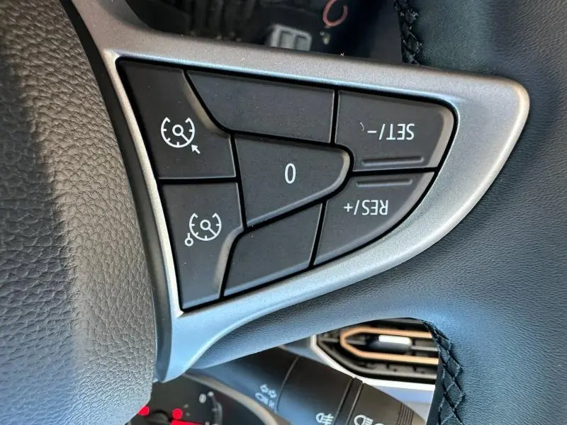 Gros plan sur les commandes de régulateur de vitesse au volant noir du Dacia Jogger blanc 2024, côté gauche.