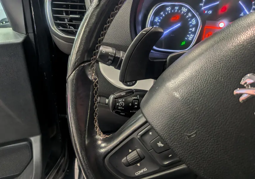 Gros plan sur le volant noir en cuir du Peugeot Expert Fourgon, avec commandes intégrées et tableau de bord éclairé en arrière-plan.