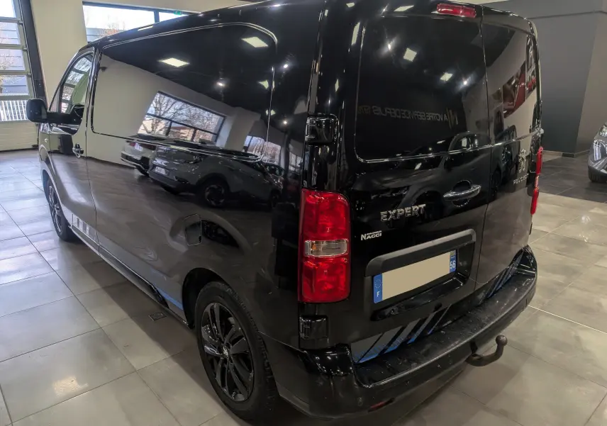 Vue 3/4 arrière droite du Peugeot Expert Fourgon noir Perla avec jantes noires et hayon double portes en intérieur showroom.