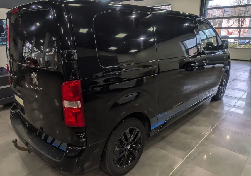 Vue 3/4 arrière droite du Peugeot Expert Fourgon noir Perla avec jantes noires et bande bleue Sport sur le bas de caisse.
