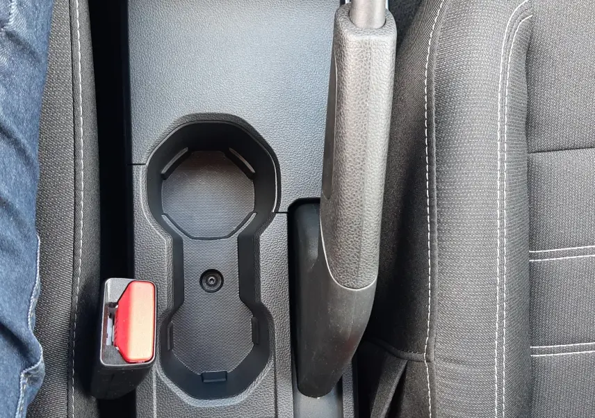 Vue plongeante sur la console centrale noire du Dacia Sandero 2024, avec frein à main, porte-gobelets et ceintures rouges.