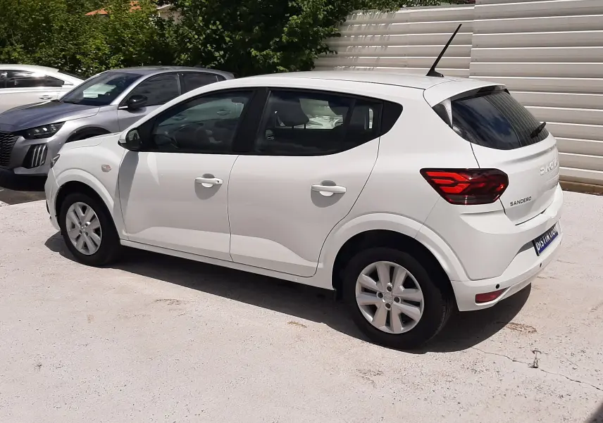 Vue 3/4 arrière droite d'une Dacia Sandero blanc glacier, compacte à cinq portes avec feux arrière rouges distinctifs.