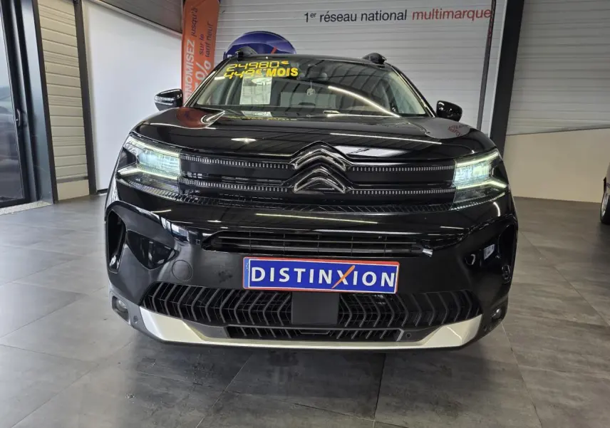 Vue avant d'un Citroën C5 Aircross noir métal avec calandre noire brillante et plaque Distinxion en intérieur showroom.