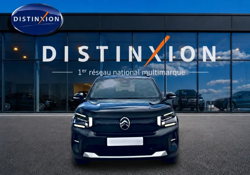 Vue frontale d'une Citroën C3 113 Plus électrique noire, avec phares LED et calandre épurée, devant un showroom Distinxion.