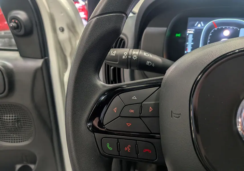 Gros plan sur la partie gauche du volant de la Fiat Panda blanc Gelato, avec commandes intégrées et tableau de bord numérique.