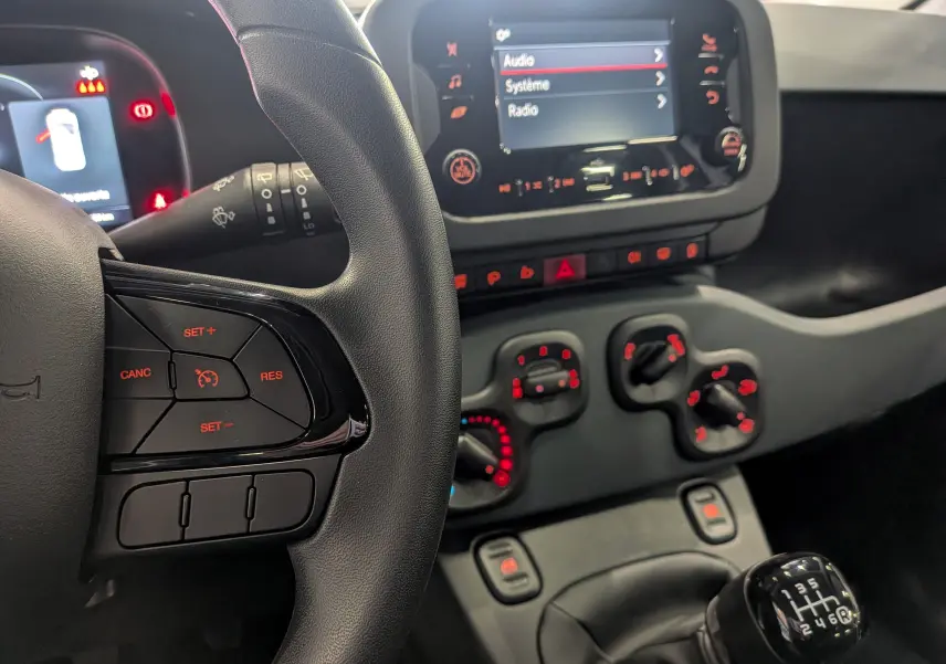 Intérieur de la Fiat Panda 1.0 Hybrid 2025 montrant le volant, la console centrale avec commandes clim et écran tactile.