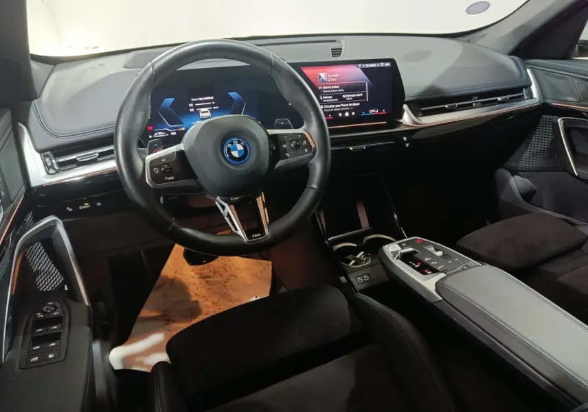 Vue intérieure du tableau de bord et volant noir du BMW X1 xDrive25e M Sport 2024 avec écran tactile central.