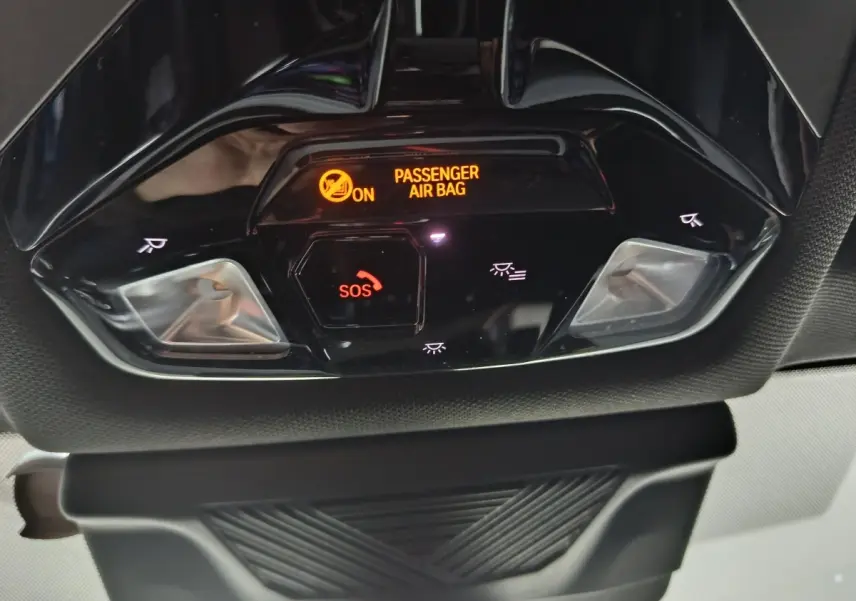 Gros plan sur la console de plafonnier noire du BMW X1 blanc, avec indicateur airbag passager et bouton SOS éclairés.