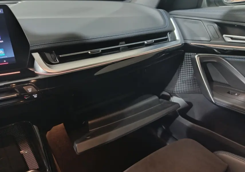 Intérieur de la BMW X1 xDrive25e 2024, vue côté passager sur la boîte à gants ouverte et tableau de bord noir.