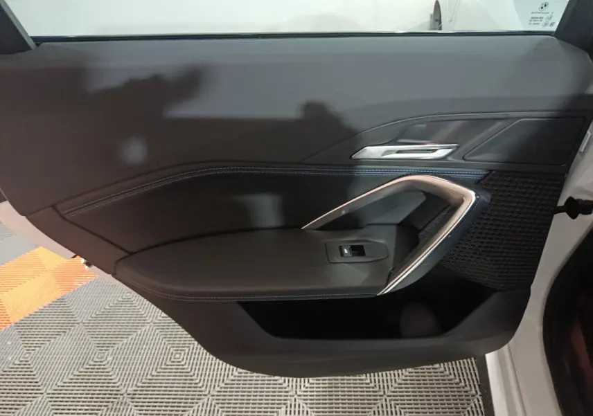 Intérieur de la porte avant gauche noire du BMW X1 xDrive25e blanc, avec poignée argentée et bouton de vitre électrique.