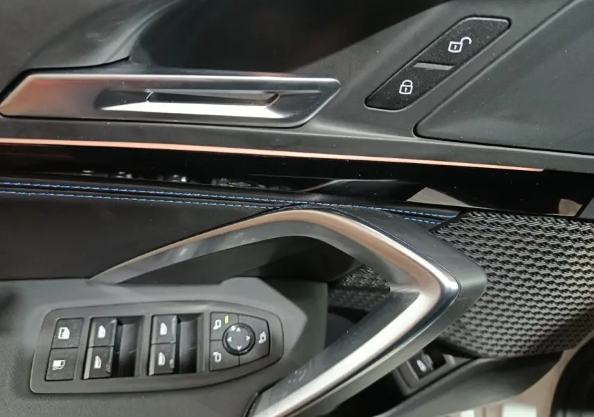 Détail intérieur côté conducteur BMW X1 xDrive25e blanc 2024, commandes vitres et poignée argentée.