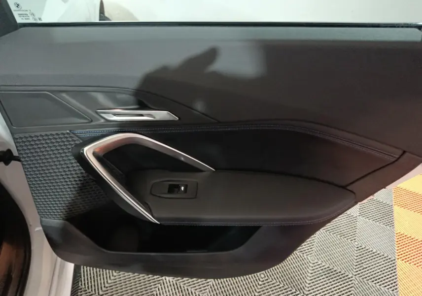 Détail de la porte intérieure côté gauche noire avec surpiqûres bleues et poignée argentée d’un BMW X1 blanc 2024.