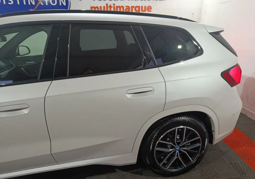 Vue latérale droite sur l'arrière d'un BMW X1 blanc avec jantes alliage et feux arrière LED visibles.
