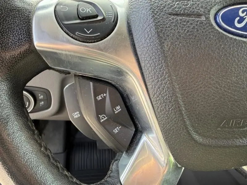 Gros plan sur le volant cuir noir du Ford Transit Connect blanc, avec commandes de régulateur de vitesse visibles.