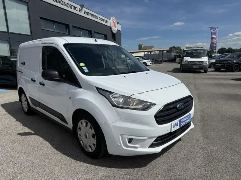 Ford Transit Connect blanc glacier vu en 3/4 avant droit, avec calandre noire et jantes acier, stationné devant un bâtiment.
