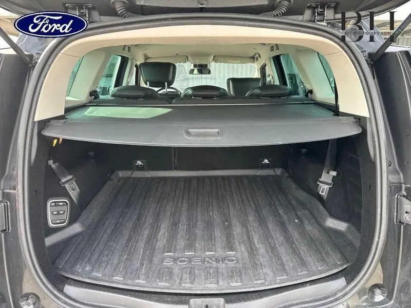 Vue arrière du coffre ouvert d'un Renault Grand Scenic noir étoilé avec cache-bagages et tapis de coffre marqué Scenic.