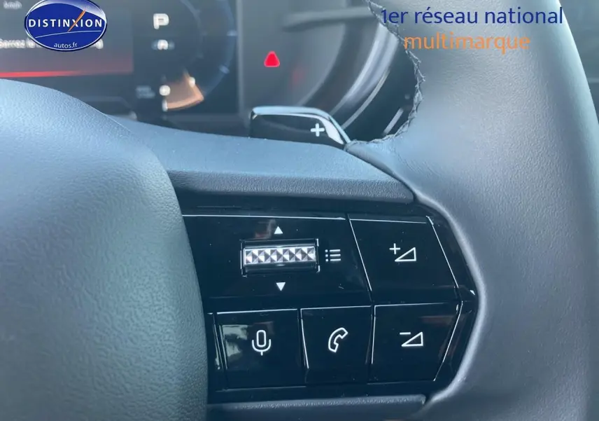 Gros plan sur les commandes au volant à gauche de l'Alfa Romeo Junior ivoire et noir, avec boutons de volume et téléphone visibles.