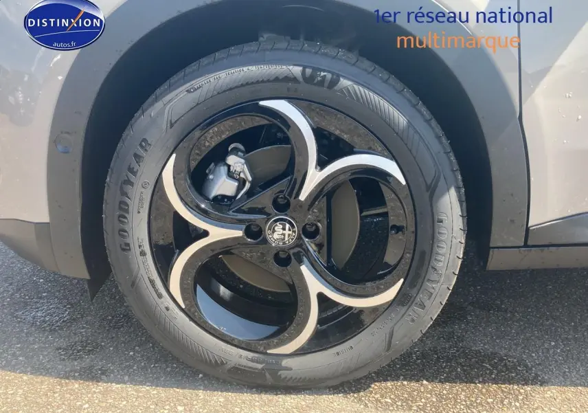 Gros plan sur la roue avant gauche de l'Alfa Romeo Junior 1.2 hybride ivoire et noir avec jante alliage noire et argentée.
