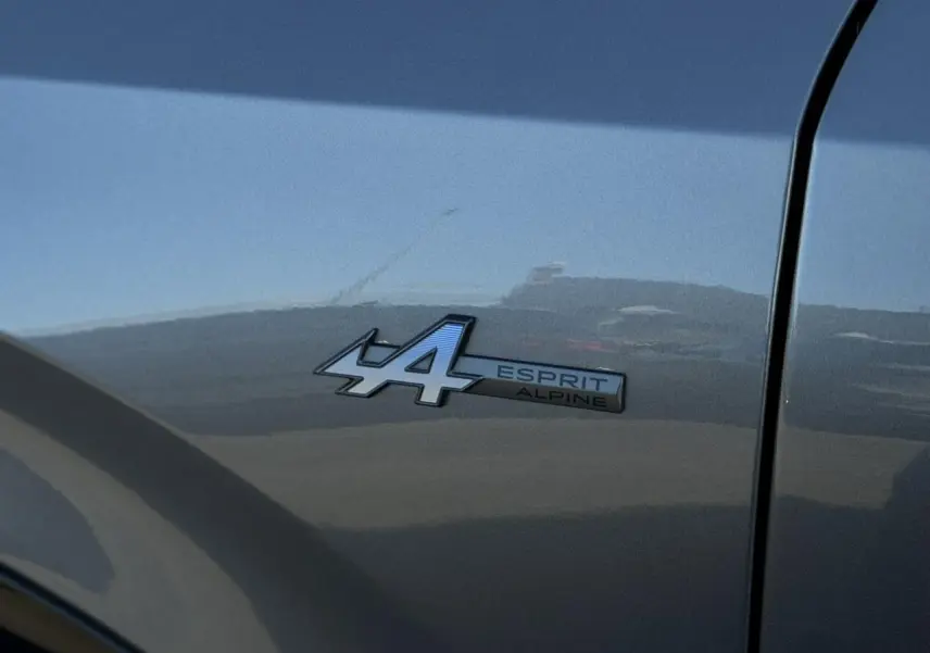 Gros plan sur le badge Esprit Alpine bleu sur la porte avant droite d’un Renault Rafale gris schiste.