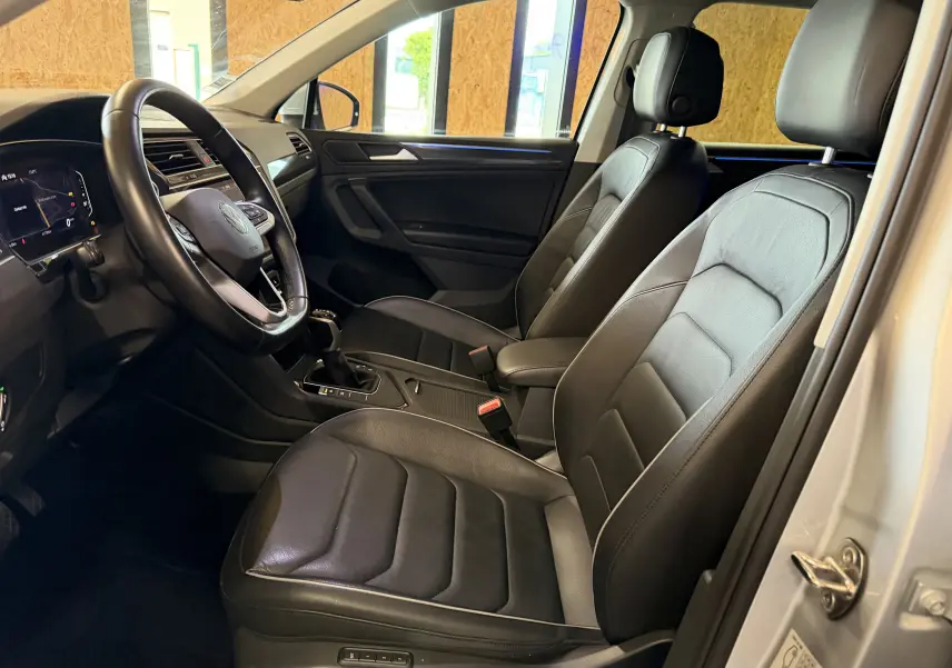 Vue intérieure côté conducteur du Volkswagen Tiguan gris clair 2022, sièges en cuir noir et tableau de bord moderne.