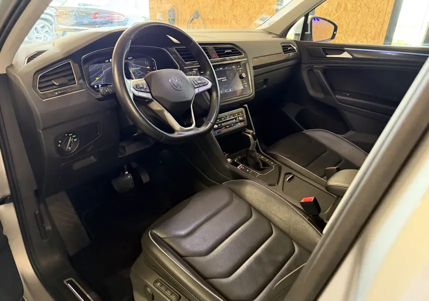 Vue intérieure côté conducteur du Volkswagen Tiguan gris clair 2022, avec volant multifonction et sièges en cuir noir.