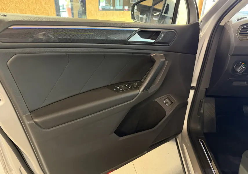 Vue intérieure de la porte avant gauche gris clair du Volkswagen Tiguan 1.4 E-HYBRID 2022 avec commandes électriques et finition noire.