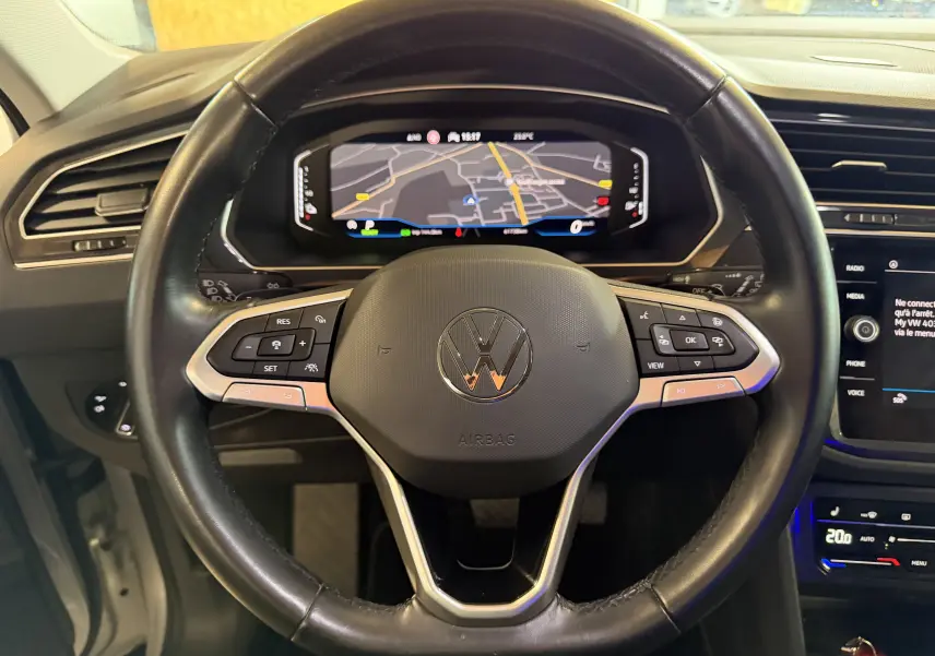 Vue rapprochée du volant cuir noir du Volkswagen Tiguan 1.4 E-HYBRID 2022 avec tableau de bord numérique affichant la navigation.
