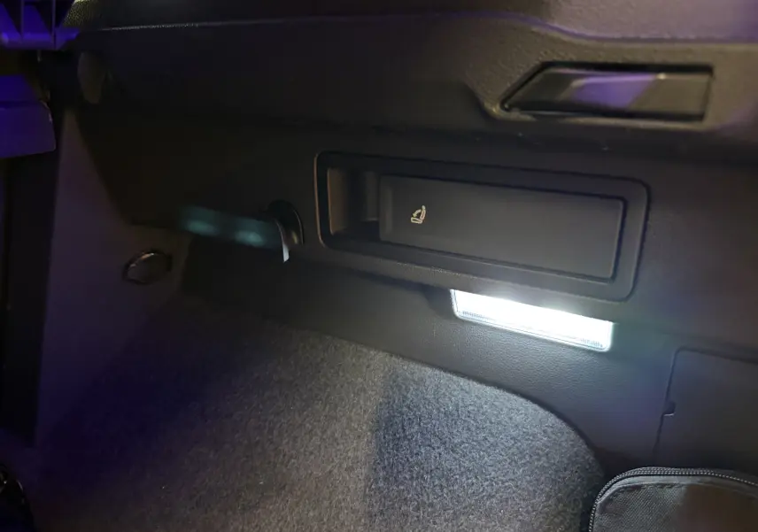 Détail intérieur du coffre du Volkswagen Tiguan 2022 gris clair, montrant le levier de rabattement des sièges et un éclairage LED.