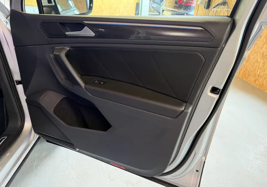 Vue rapprochée de la porte avant gauche noire du Volkswagen Tiguan gris clair 2022, avec insert décoratif et bouton de vitre électrique.