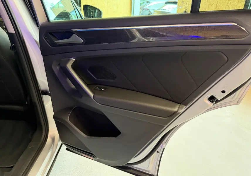 Vue intérieure de la porte arrière droite du Volkswagen Tiguan gris clair, avec garniture noire et poignée angulaire.