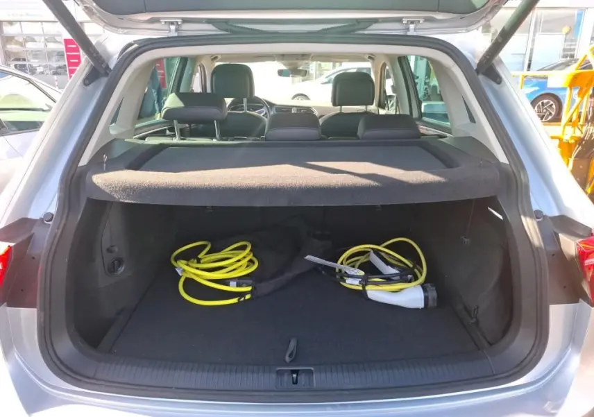 Vue arrière du coffre ouvert d'un Volkswagen Tiguan gris clair 2022, avec câbles de recharge hybride visibles à l'intérieur.