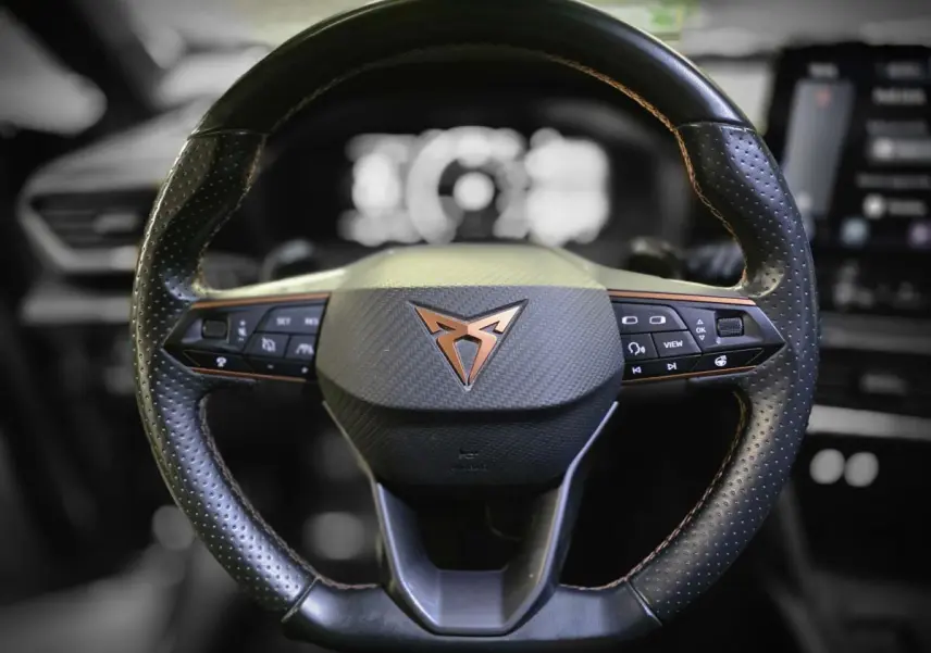 Volant sport noir perforé avec surpiqûres cuivre et logo CUPRA en cuivre au centre, vue frontale rapprochée.