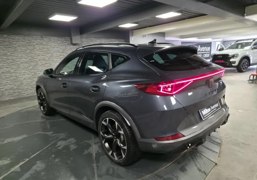 Vue 3/4 arrière droite du CUPRA Formentor gris avec bandeau LED arrière et jantes alliage noires en intérieur showroom.