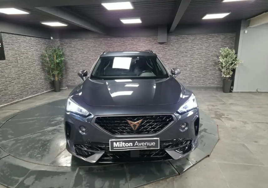 Vue avant d'un CUPRA Formentor gris avec calandre noire et logo cuivre, dans un showroom intérieur.