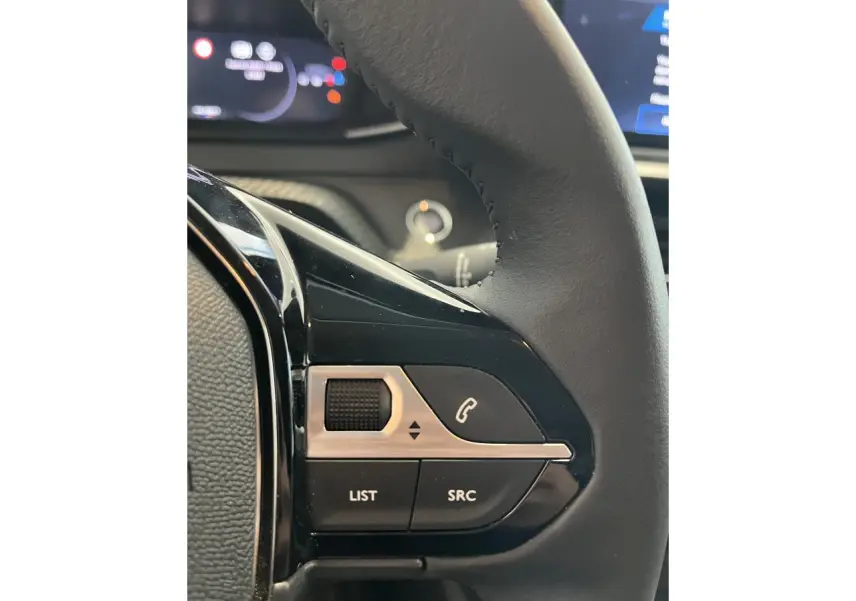 Gros plan sur les commandes multimédia à gauche du volant cuir d'une Peugeot 208 gris clair Selenium 2024.