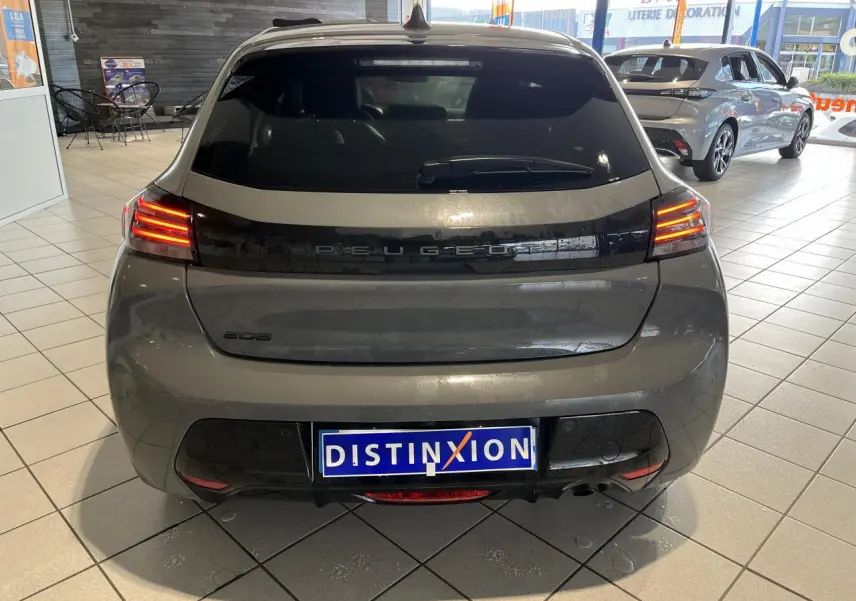 Vue arrière d'une Peugeot 208 gris clair Selenium avec bandeau noir brillant et feux arrière à LED en intérieur de showroom.