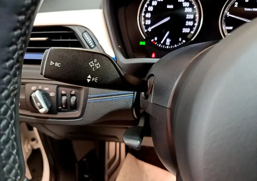 Gros plan sur le commodo gauche et le tableau de bord noir avec compteurs blancs du BMW X1 sDrive18i M Sport 2022.