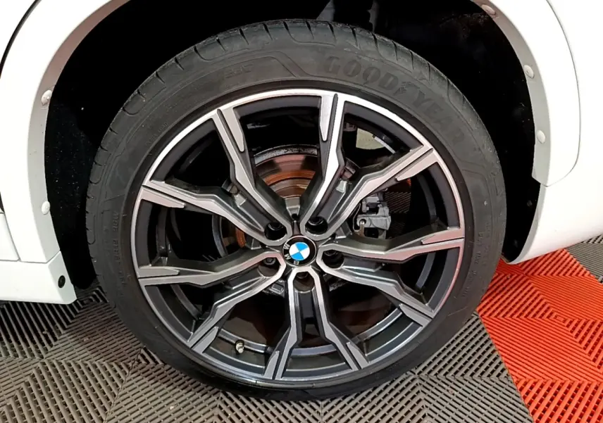 Gros plan sur la roue avant droite d’un BMW X1 blanc, jante alliage noire et argent avec logo BMW central.