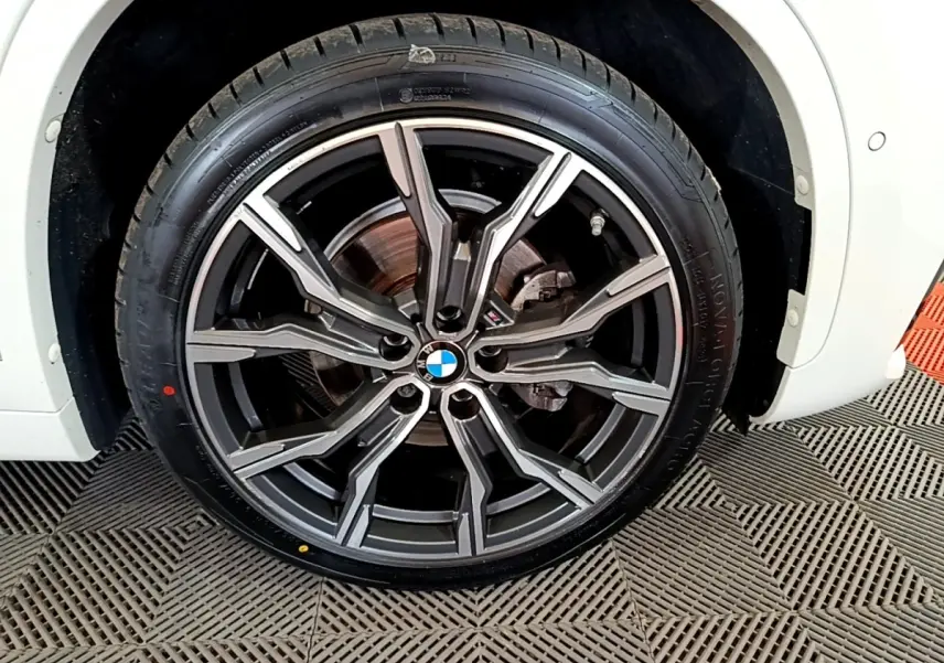 Gros plan sur la roue avant droite d'un BMW X1 blanc, avec jante alliage M Sport à design étoilé.
