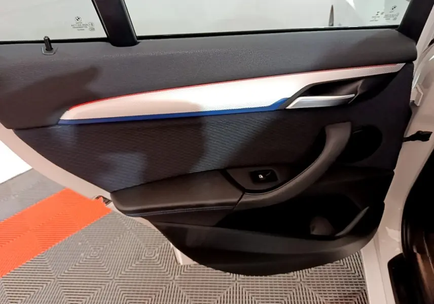 Vue rapprochée de la porte arrière droite blanche d’un BMW X1 2022 avec insert décoratif tricolore et poignée noire.