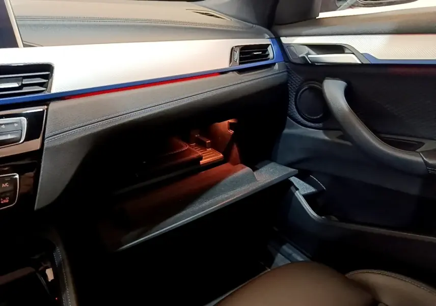 Intérieur côté passager du BMW X1 blanc 2022, vue sur boîte à gants ouverte et détails du tableau de bord noir et argent.