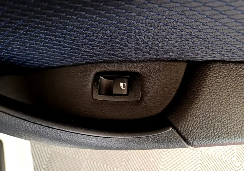Bouton de commande de lève-vitre intégré dans la garniture intérieure noire d'une BMW X1 blanche, vue en gros plan.