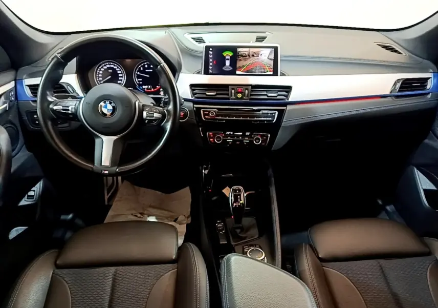 Vue intérieure avant du tableau de bord noir et volant cuir d’une BMW X1 sDrive18i M Sport 2022 avec écran tactile central.