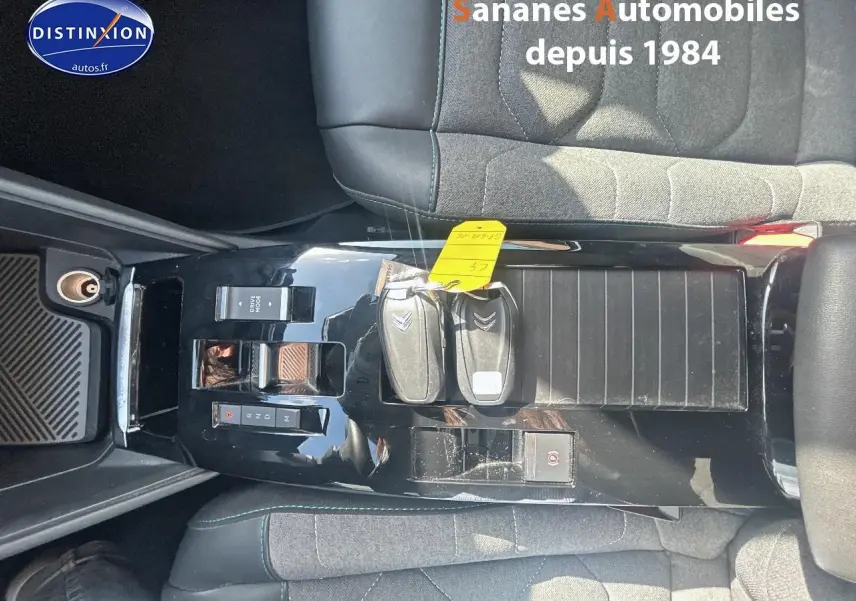 Vue plongeante sur la console centrale noire brillante de la Citroën C4 avec clés et sièges tissu gris et cuir noir.