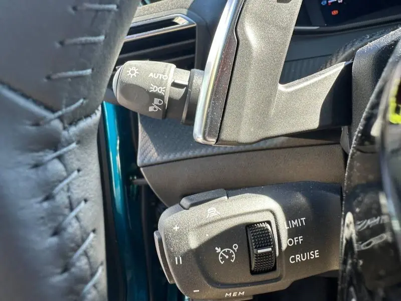 Gros plan sur les commandes de régulateur de vitesse et éclairage, avec une partie de la portière bleu obsession visible côté gauche.