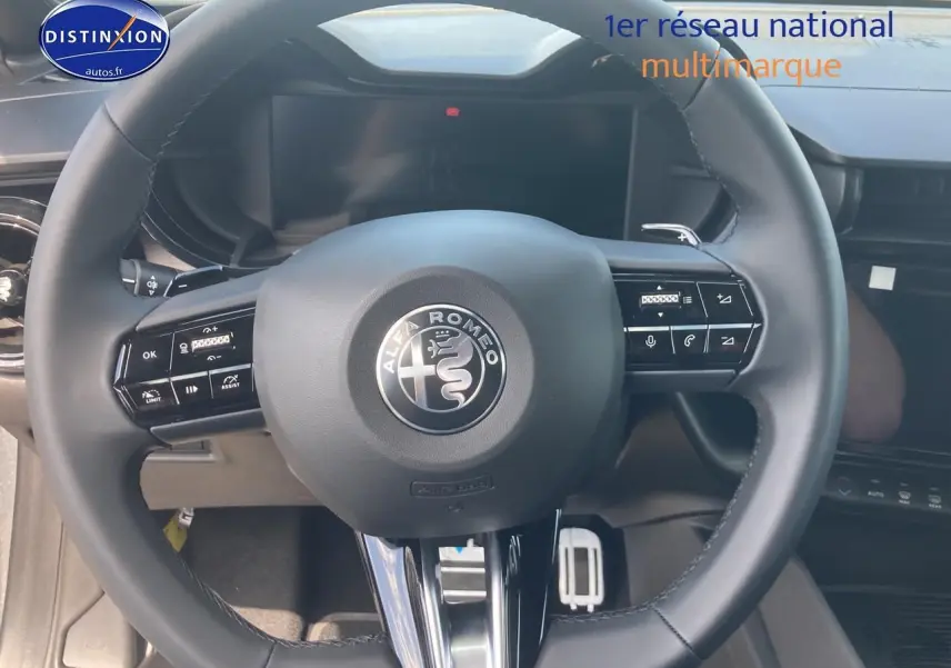 Vue rapprochée du volant noir de l'Alfa Romeo Junior 1.2 hybride 2026 avec commandes intégrées et logo central.